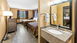 Habitación de hotel con cama, escritorio, ventana con cortinas y baño con lavamanos y espejo.