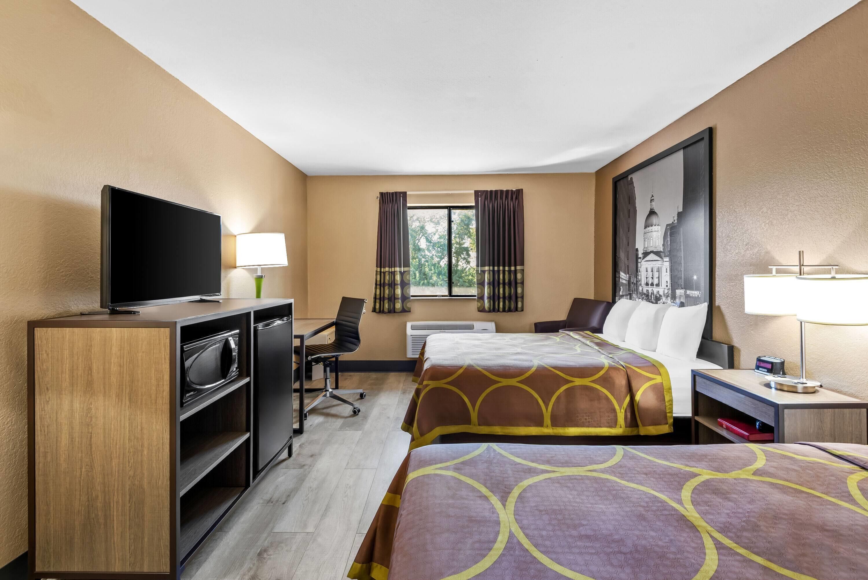 A hotel room with two beds, a TV, a desk, and a chair.