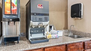 Una máquina de café con opciones para jugo de naranja y manzana, un dispensador de café y un lavamanos con dispensador de jabón.
