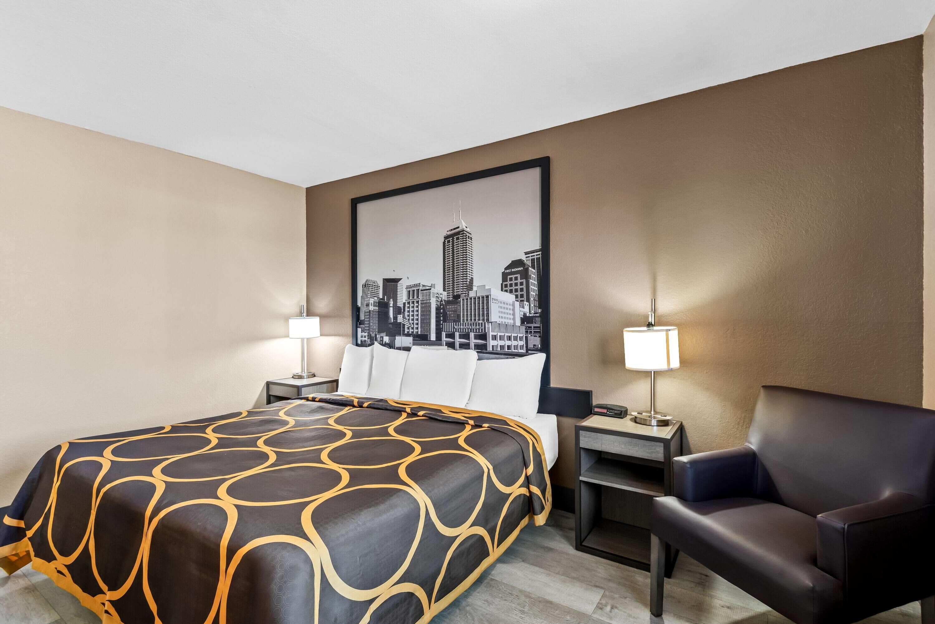 Una habitación de hotel con cama, una silla, un escritorio y un cuadro de paisaje urbano en la pared.