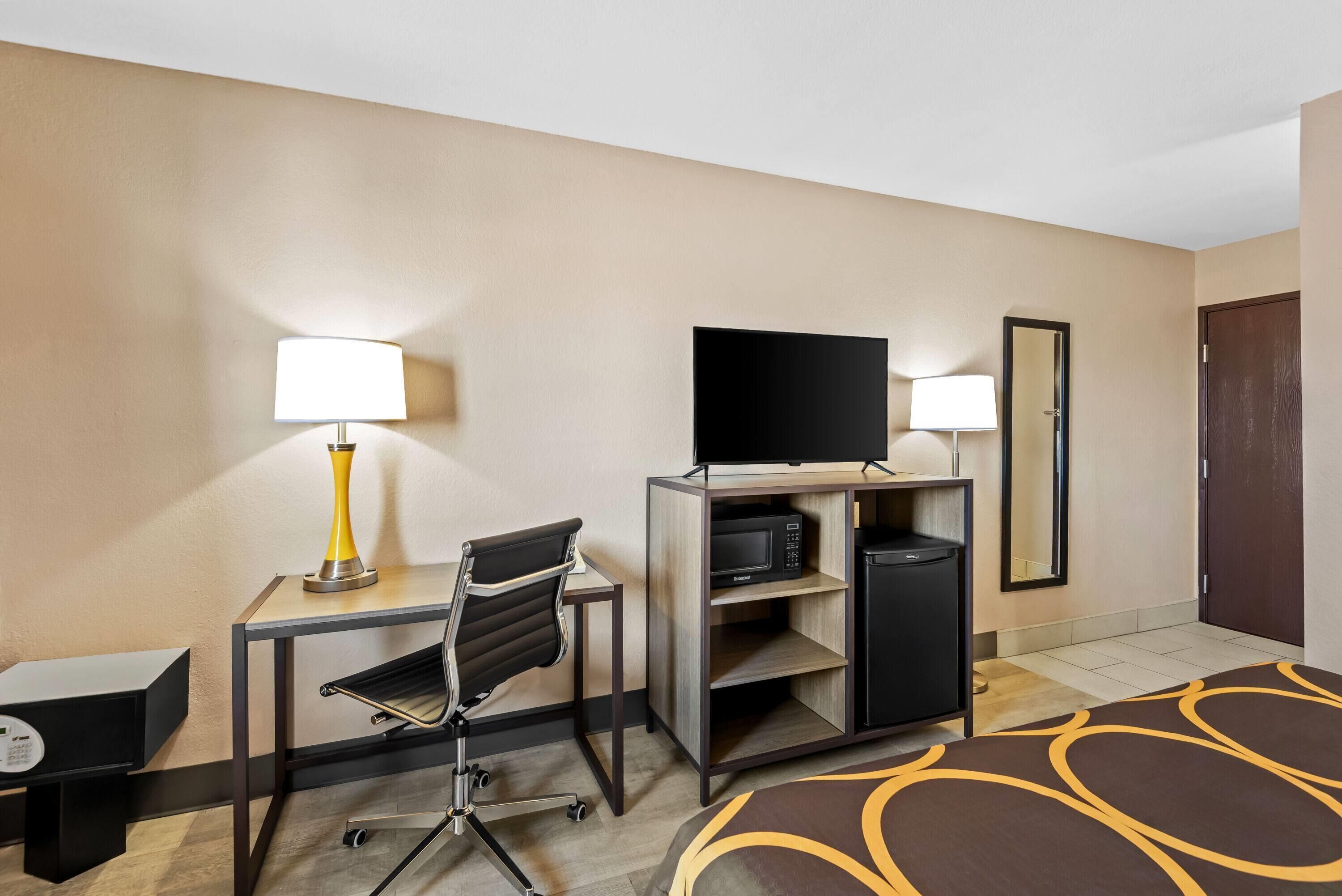 A hotel room with a desk, chair, television, and a mirror.