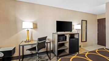 A hotel room with a desk, chair, television, and a mirror.