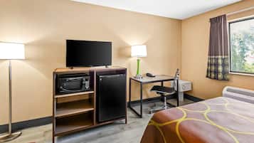 Habitación de hotel con cama, escritorio, computadora, teléfono, televisor, microondas y refrigerador pequeño.