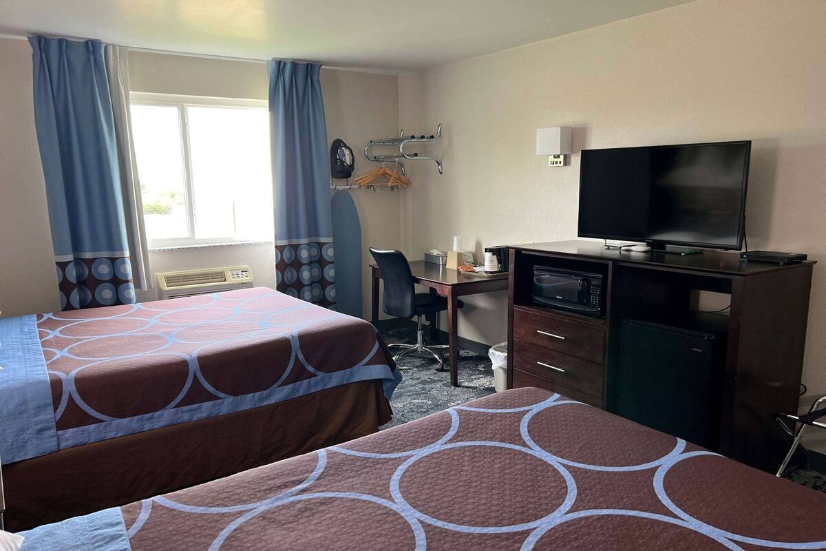 A hotel room with two beds, a desk with a computer, a TV, and a microwave.
