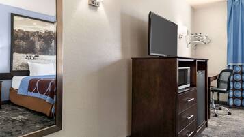 A hotel room with a bed, a television on a wooden cabinet, a desk with a chair, and a bathroom with a shower and grab bar.