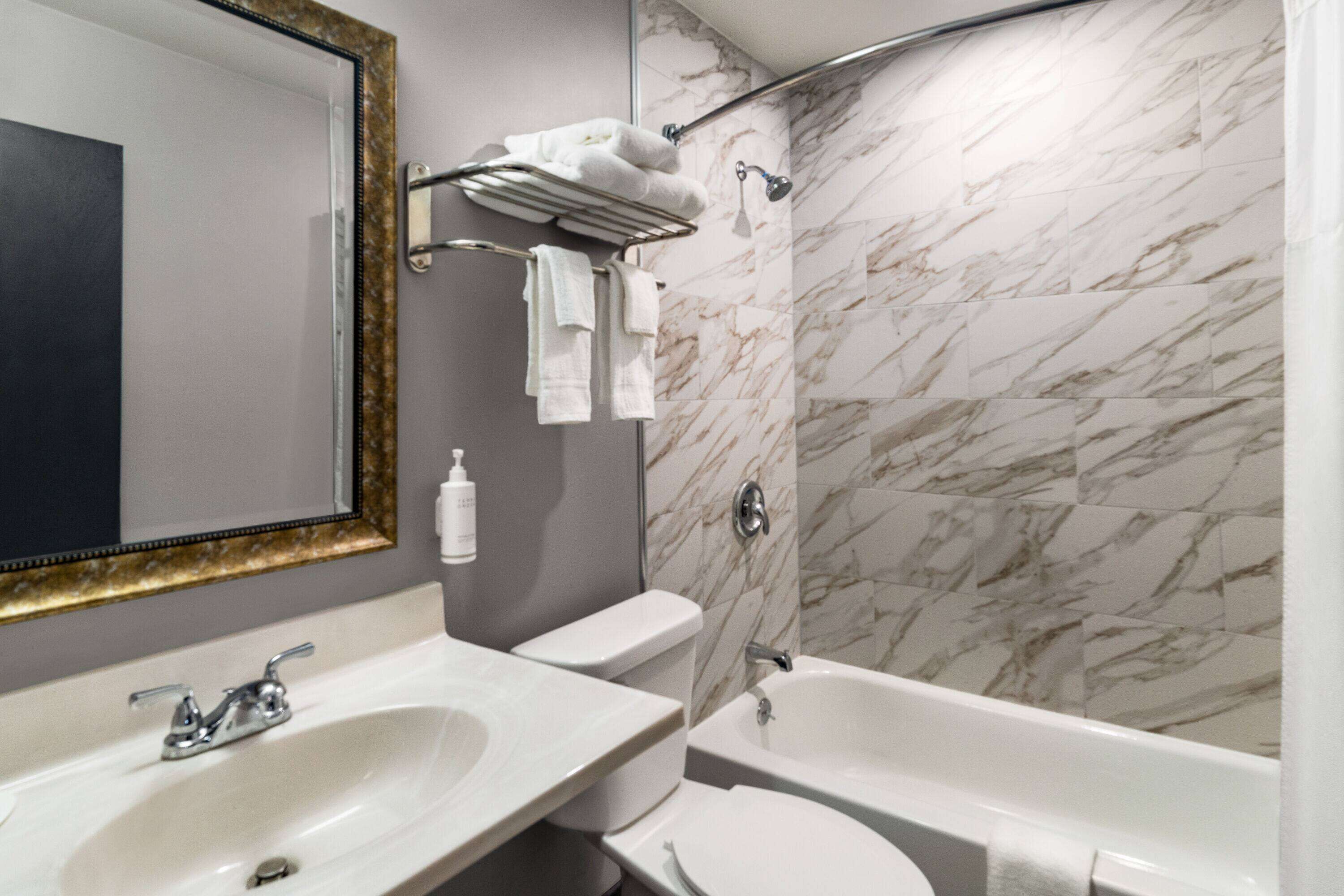 Un bany amb paret de marbre, un lavabo, un vàter i una banyera.