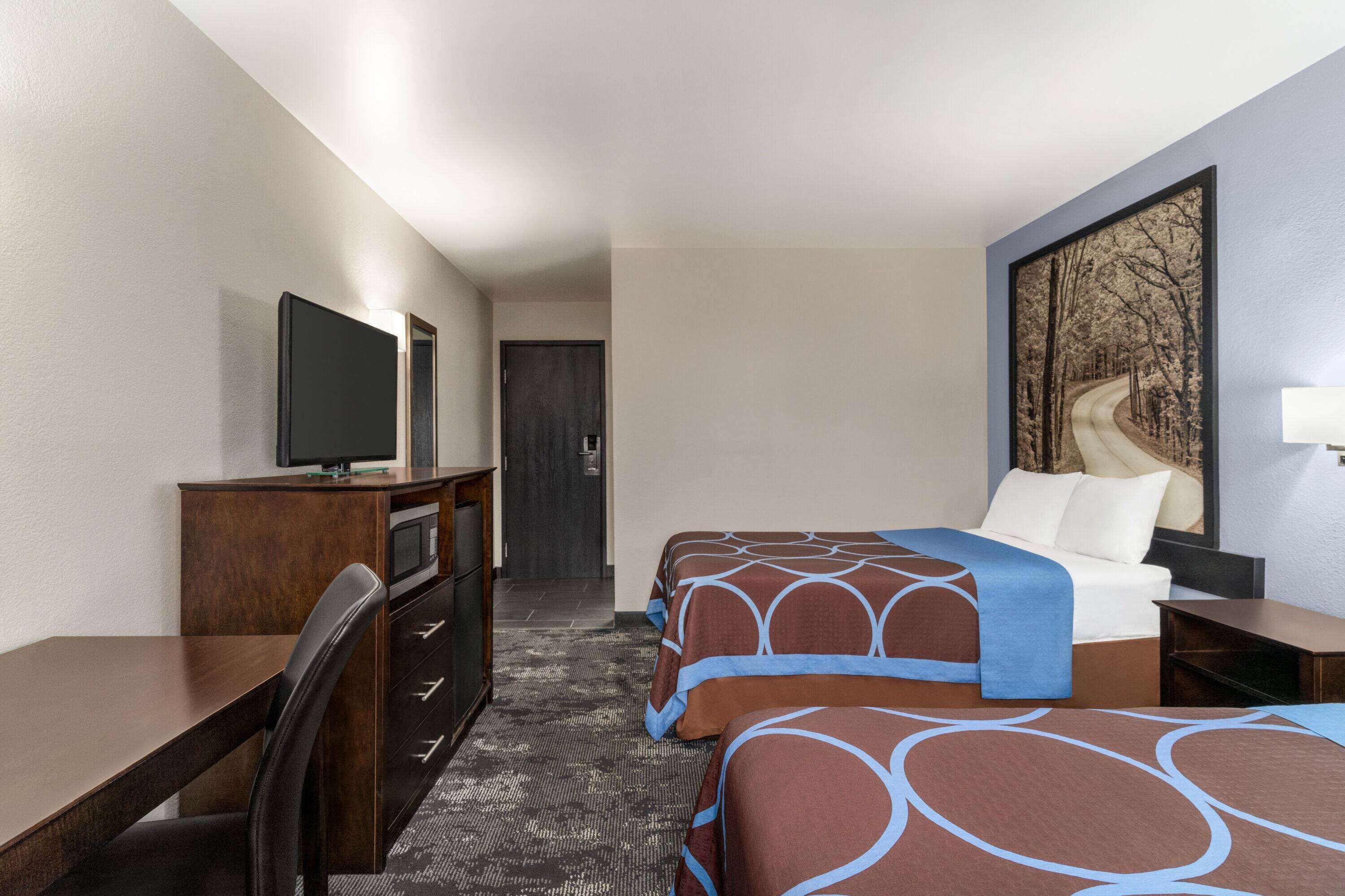 A hotel room with two beds, a desk, a television, and a large painting on the wall.