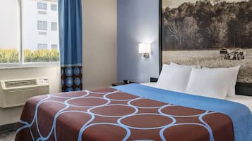 Habitación de hotel con una cama grande, una ventana que ofrece vistas a un edificio, un aire acondicionado de pared y un cuadro de un campo con un vehículo.