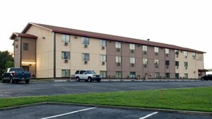 A multi-story hotel with a flat roof, parking lot, and a grassy area in front. - The Lodge at Pensacola (Pensacola)
