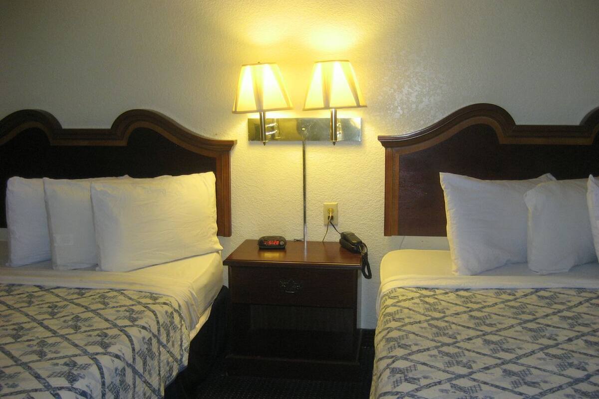 A hotel room with two beds, a nightstand with a lamp, and a phone.