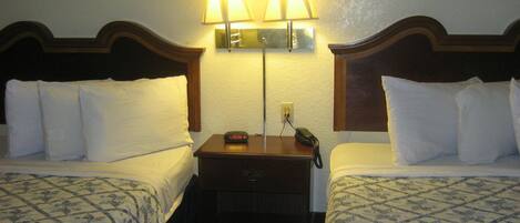Habitación de hotel con dos camas, una mesita de noche con lámpara y un teléfono.