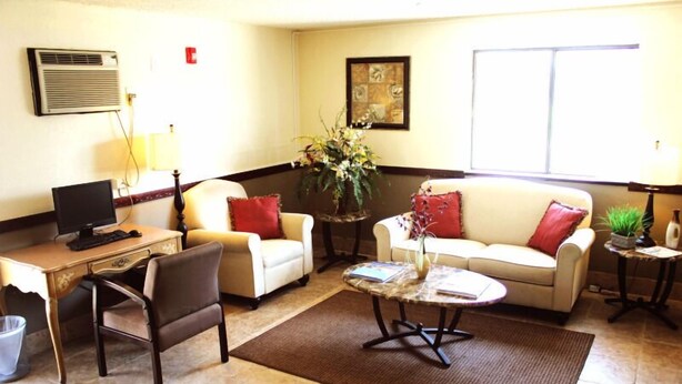 A living room with a desk, two armchairs, a coffee table, and a sofa with red cushions. There is a potted plant on a side table and a framed artwork on the wall. - The Lodge at Pensacola (Pensacola)