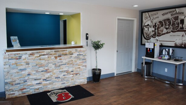 A reception area with a brick wall, a blue accent wall, a reception desk, a potted plant, a door, and a wall-mounted coffee machine. - Super 8 by Wyndham Warner Robins (Warner Robins)