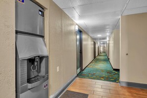 A hotel hallway with a push button trash bin, a carpeted floor, and a wooden floor at the end. - Super 8 by Wyndham Warner Robins (Warner Robins)