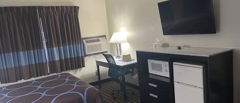 A hotel room with a bed, a desk, a television, and a minibar.