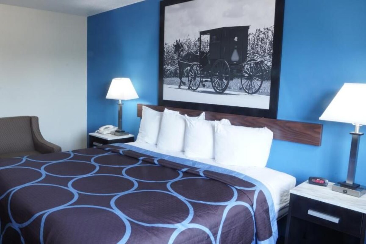 Ein Hotelzimmer mit einem Bett, zwei Nachttischen, einem Sessel und einem gerahmten Bild an der Wand.