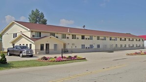 Um motel com um prédio de dois andares, área de estacionamento coberta e um pequeno jardim com flores.