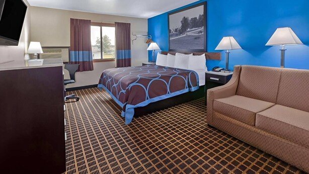 Quarto de hotel com cama, mesa de trabalho com televisão, sofá e janela com cortinas.
