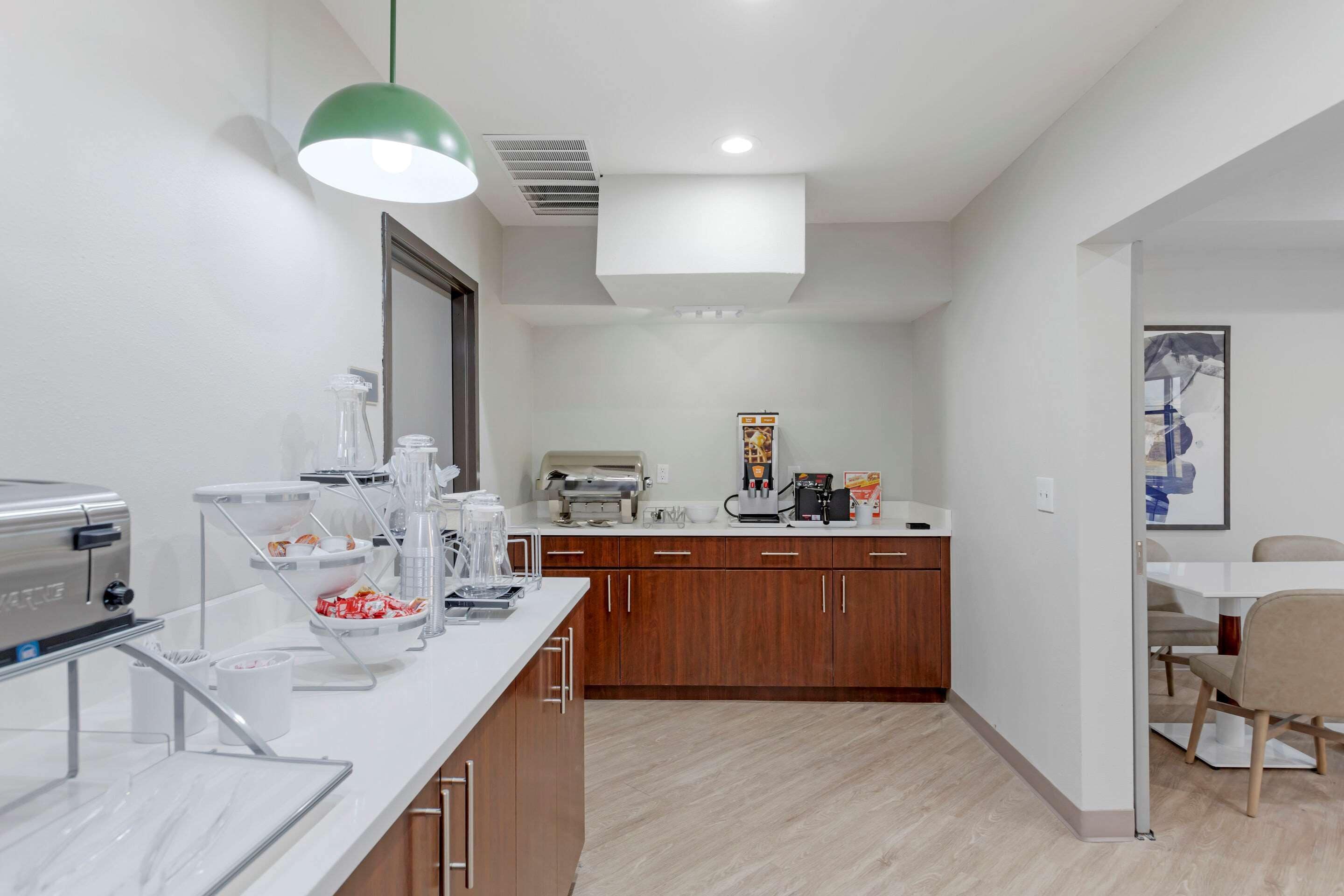 A modern kitchen with a white countertop, wooden cabinets, and a coffee station.