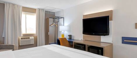 Quarto de hotel com cama, escrivaninha com cadeira, televisão de tela plana na parede, janela com cortinas e ar condicionado instalado.