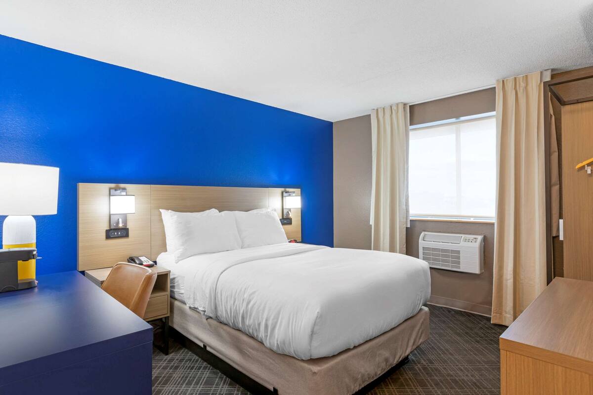 A hotel room with a large bed, bedside tables, a desk, and a window with curtains.
