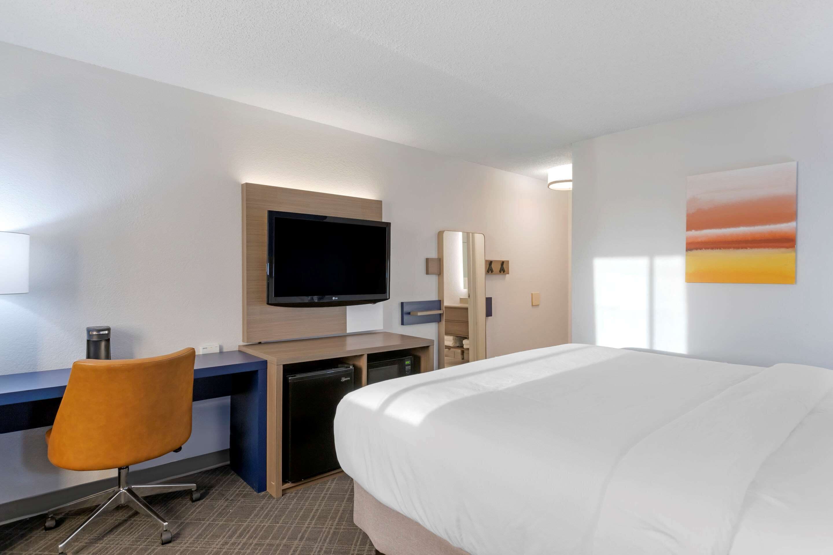 Habitación de hotel con cama, escritorio, silla, televisor y un cuadro en la pared.