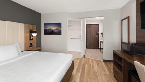 Una habitación de hotel con cama, mesita de noche, lámpara y vistas al exterior.