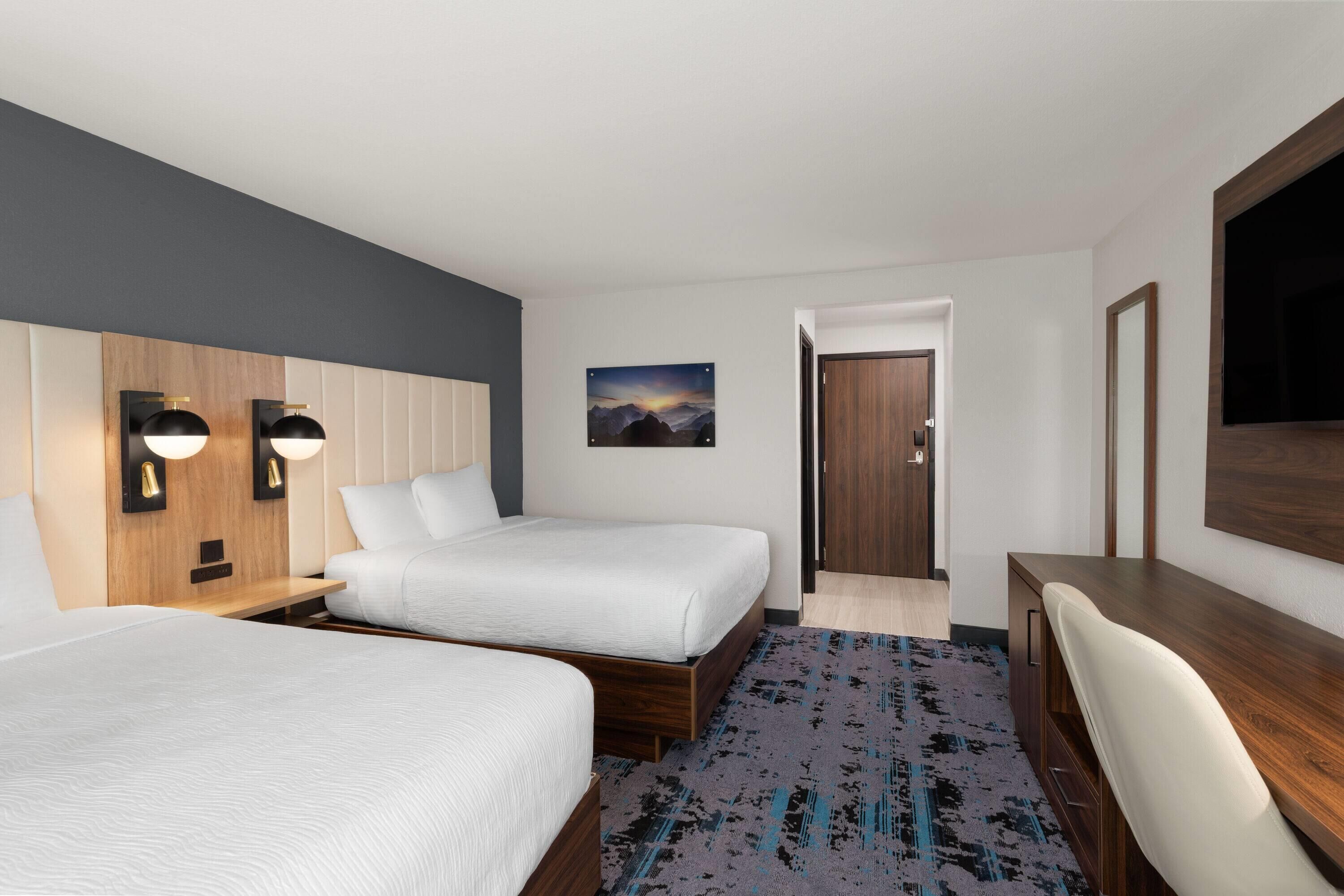 A hotel room with two beds, a desk, a chair, a TV, and a painting on the wall.