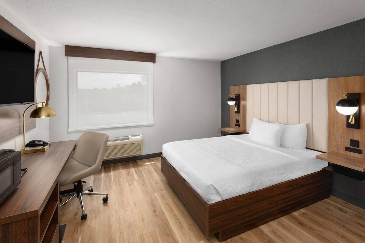 A modern hotel room with a wooden bed, a desk, and a chair.