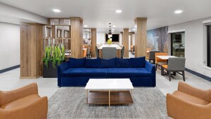 Un lobby moderno con un sofá azul, columnas de madera, una mesa de centro blanca y un área de comedor al fondo.