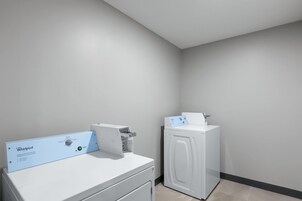 Un lavadero con lavadora y secadora de carga frontal, un panel de control y una secadora montada en la pared.