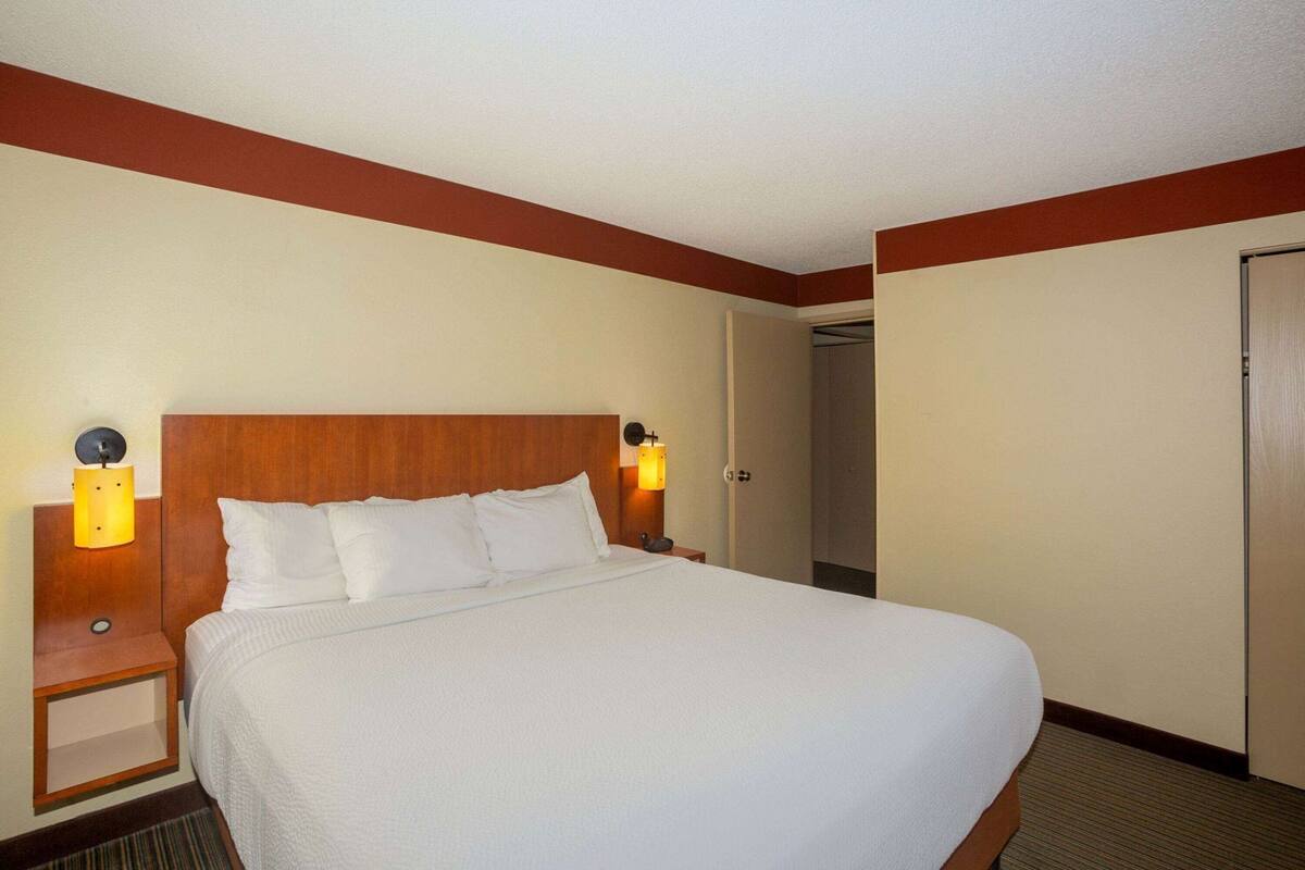 A hotel room with a large bed, two bedside lamps, a wooden headboard, and a door leading to a closet.