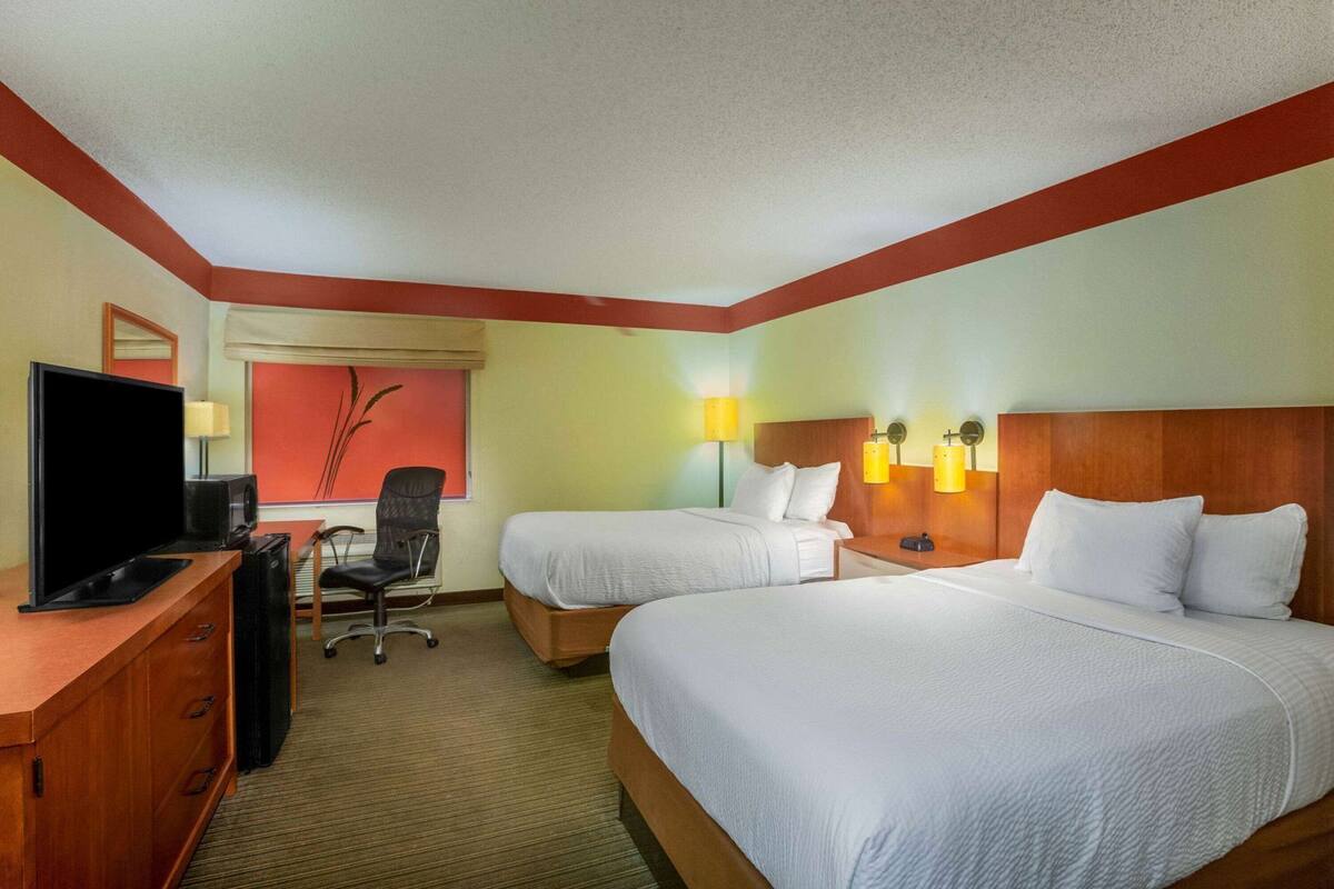 A hotel room with two beds, a desk with a TV, a chair, and a lamp.