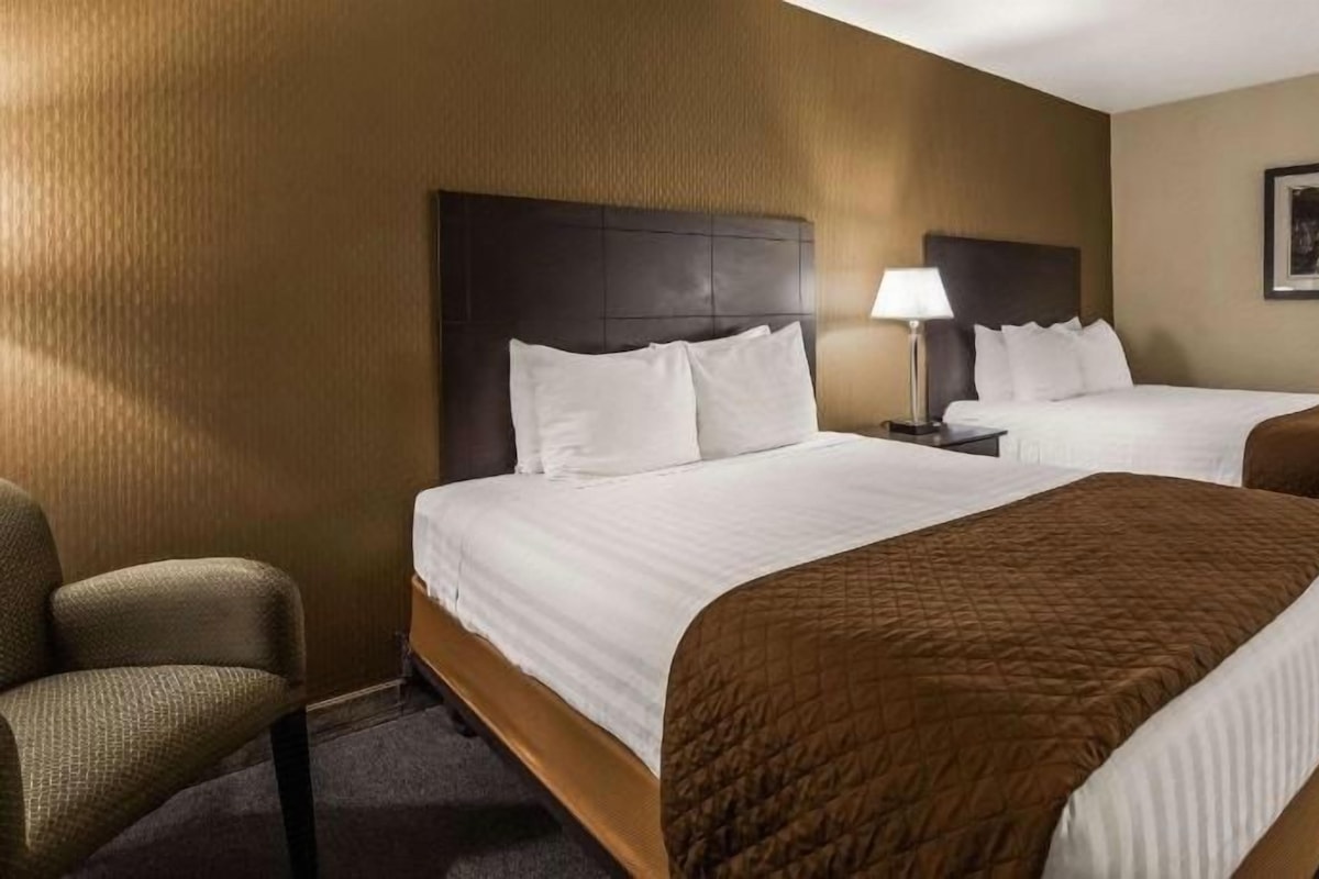 Une chambre d’hôtel avec deux lits, une chaise, une table de chevet et une lampe.