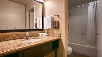 A bathroom with a granite countertop sink, a mirror, a towel dispenser, and a shower with a curtain.
