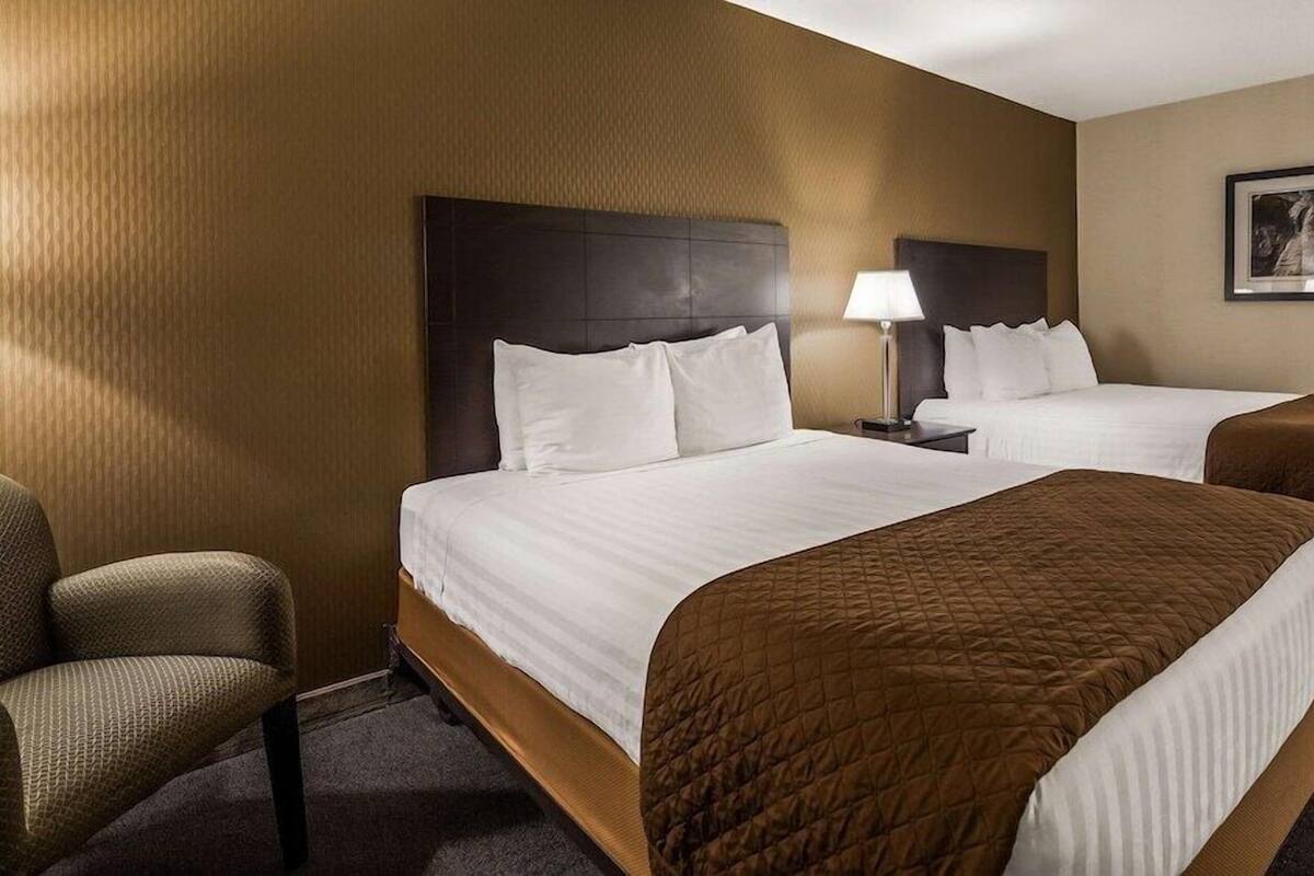 Ein Hotelzimmer mit zwei Betten, einem Sessel, einer Lampe und einem gerahmten Bild an der Wand.