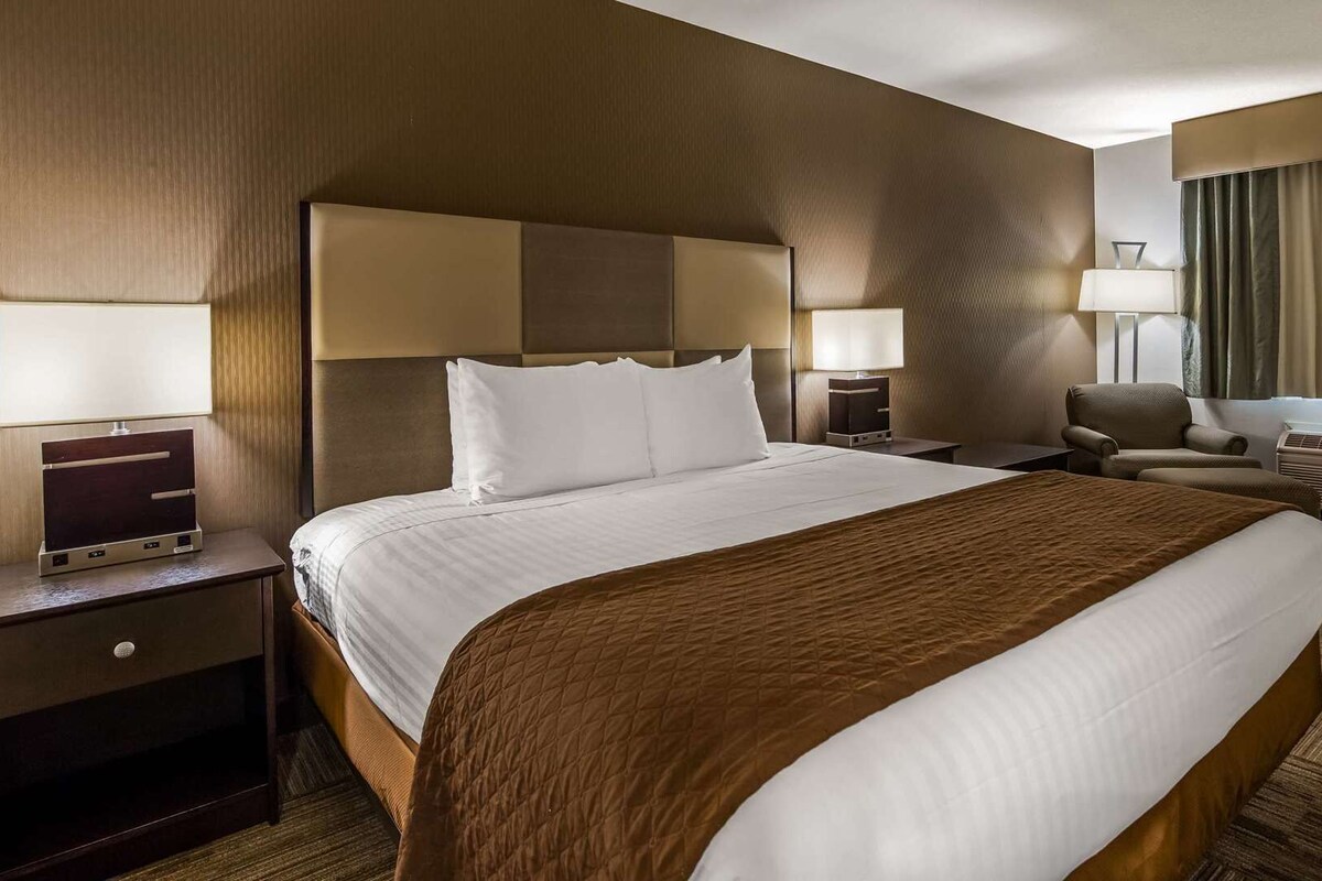 Una habitación de hotel con una cama grande, dos mesitas de noche, una silla, un escritorio y una lámpara.