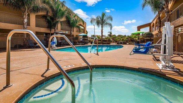 Piscina com água azul cristalina, rodeada por espreguiçadeiras e guarda-sóis, com um edifício ao fundo.