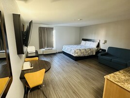 Habitación de hotel con cama, escritorio con silla, televisión, sofá y ventana con cortinas.