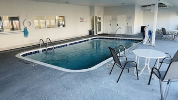 An indoor swimming pool with clear water, surrounded by lounge chairs and a tiled floor.