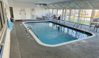 Una piscina interior con normas claramente expuestas, un área de estar cubierta con sillas y vistas al exterior a través de amplias ventanas.