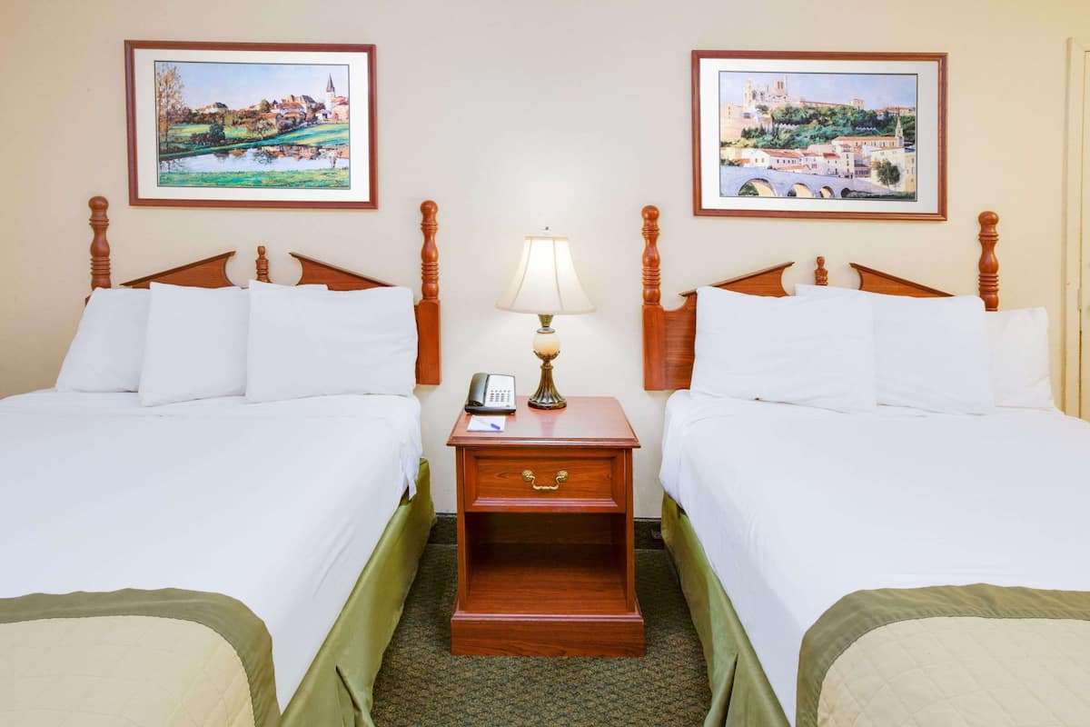 Quarto de hotel com duas camas de solteiro, mesa de cabeceira com luminária, telefone e gaveta.