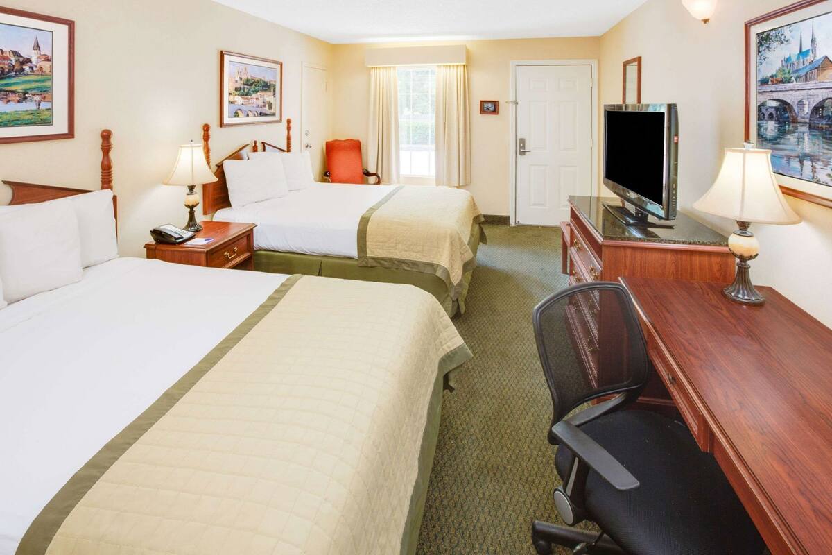 Quarto de hotel com duas camas, uma mesa com televisão, uma cadeira e uma janela com cortinas.