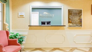 A reception area with a Baymont Inn & Suites sign, a check-in counter, a red chair, and a wall-mounted signboard. - Baymont by Wyndham Ozark (Ozark)