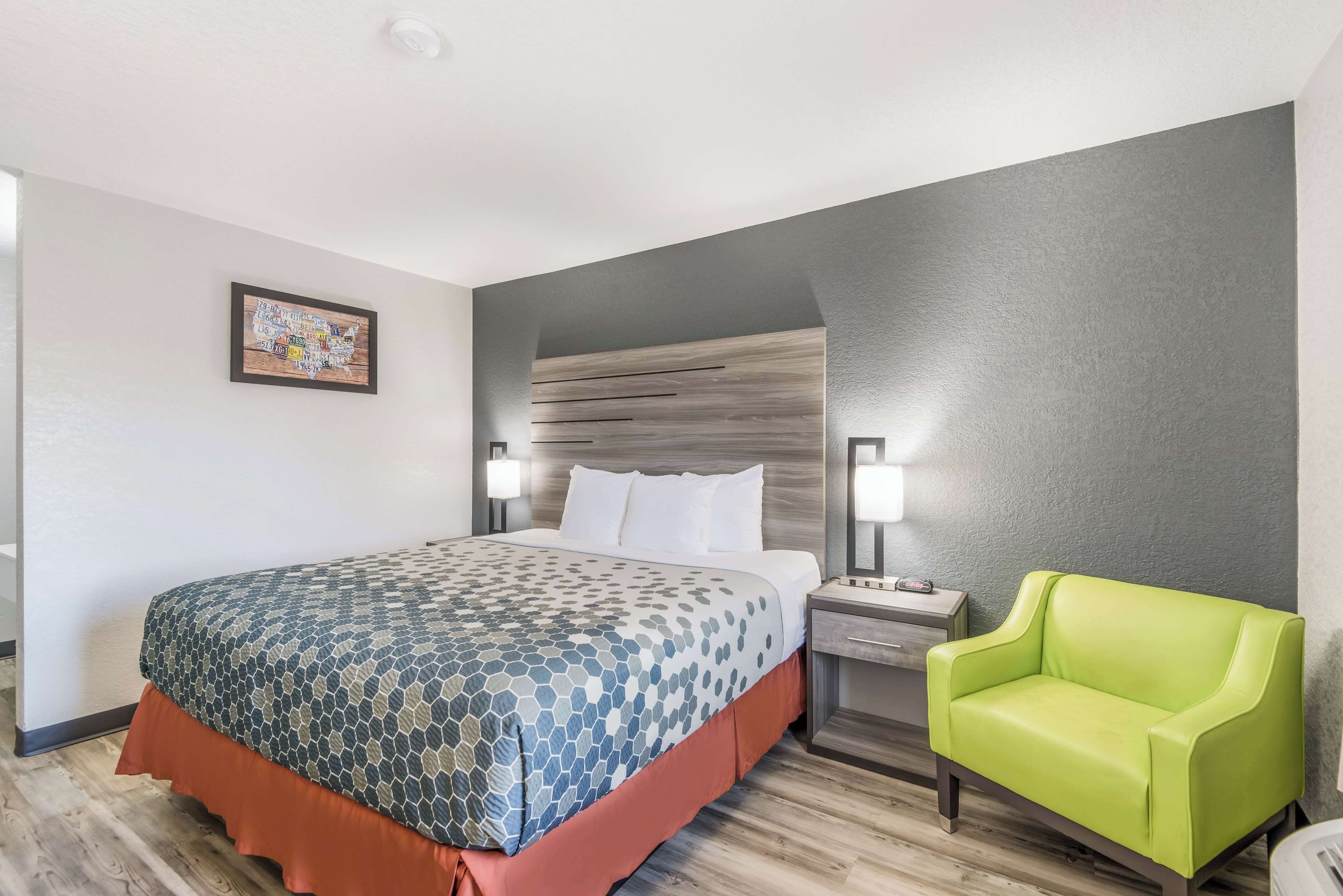 Una habitación de hotel con una cama, una mesita de noche, un sillón verde y una obra de arte colgada en la pared.
