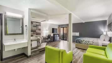 A modern hotel room with a large bed, a desk, a chair, and a bathroom with a sink and mirror.