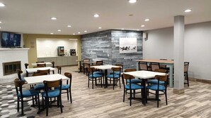 A restaurant with multiple tables and chairs, a kitchen area, and a stone accent wall. - Sonesta Essential Des Moines (Des Moines)