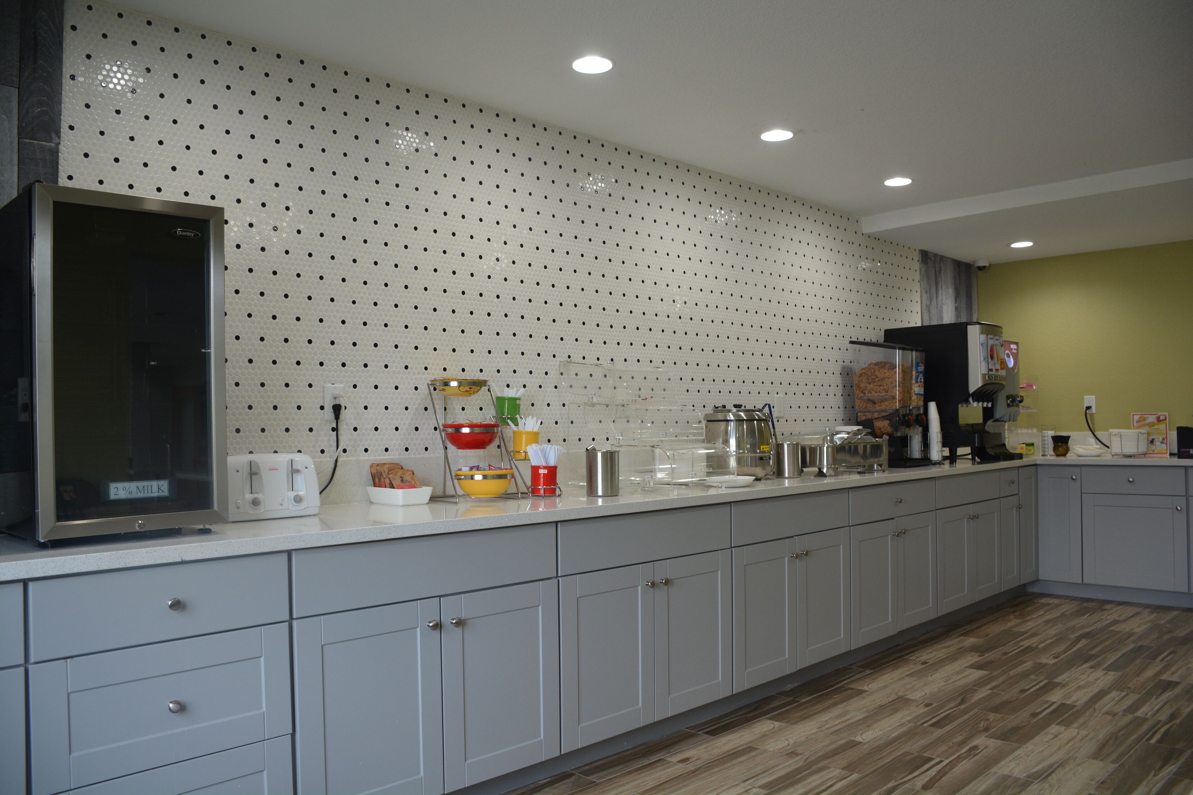A modern kitchen with grey cabinets, a stainless steel refrigerator, and a perforated backsplash.