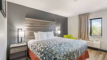 A modern hotel room with a large bed, a nightstand, a chair, and a window with curtains.