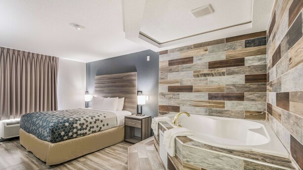 A modern hotel room with a large bed, a built-in desk, a vanity with a bathtub, and a large window with curtains. - Sonesta Essential Des Moines (Des Moines)